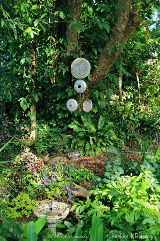 The mobile, made from stump caps and aluminium pot-lids, creates a vertical element at the junction of the gravel and leaf-paths.